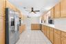 Kitchen featuring natural wood cabinetry, stainless steel refrigerator, white countertops, tile flooring, and dual ceiling fans