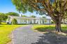 Single-story residence featuring a curved paved driveway, exterior shutters, attached garage, and mature landscaping on a spacious lot