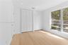 Room interior featuring wood-finish flooring, white walls, dual louvered-door closets, and multi-pane windows with exterior greenery