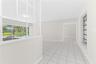 Interior space featuring white ceramic tile flooring, a half-wall with a white-frame glass partition, and large windows with horizontal mullions