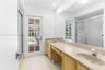 Bathroom featuring an extended vanity with dual integrated sinks, stone-finish countertops, full-width wall mirror, and a glass-enclosed shower