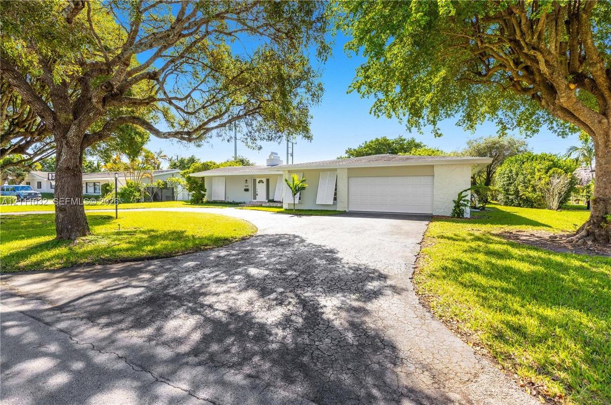 Single-story residence featuring a painted brick exterior, attached two-car garage, operable exterior shutters, and a paved driveway, set on a lot wit