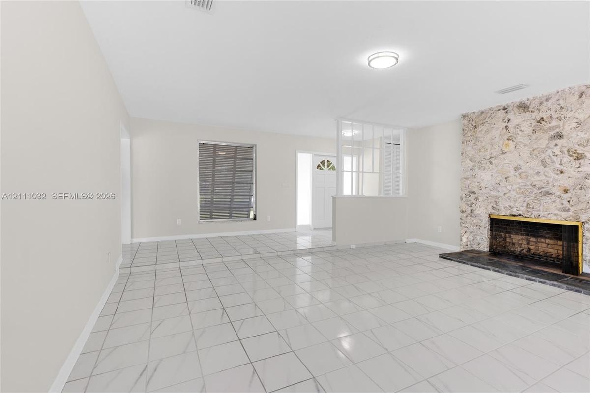Living space featuring large-format tile flooring, a floor-to-ceiling natural stone fireplace, dark stone hearth, and a white grid-pattern partition s