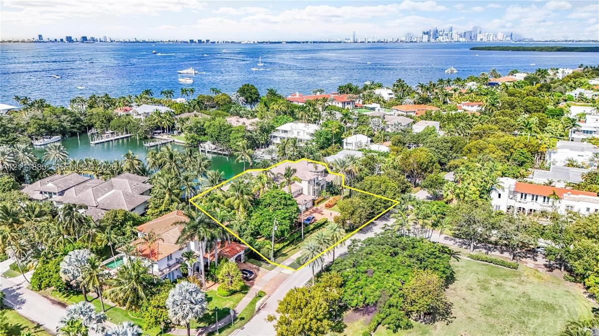 Aerial perspective of waterfront property featuring mature landscaping, paved driveway, and proximity to open water