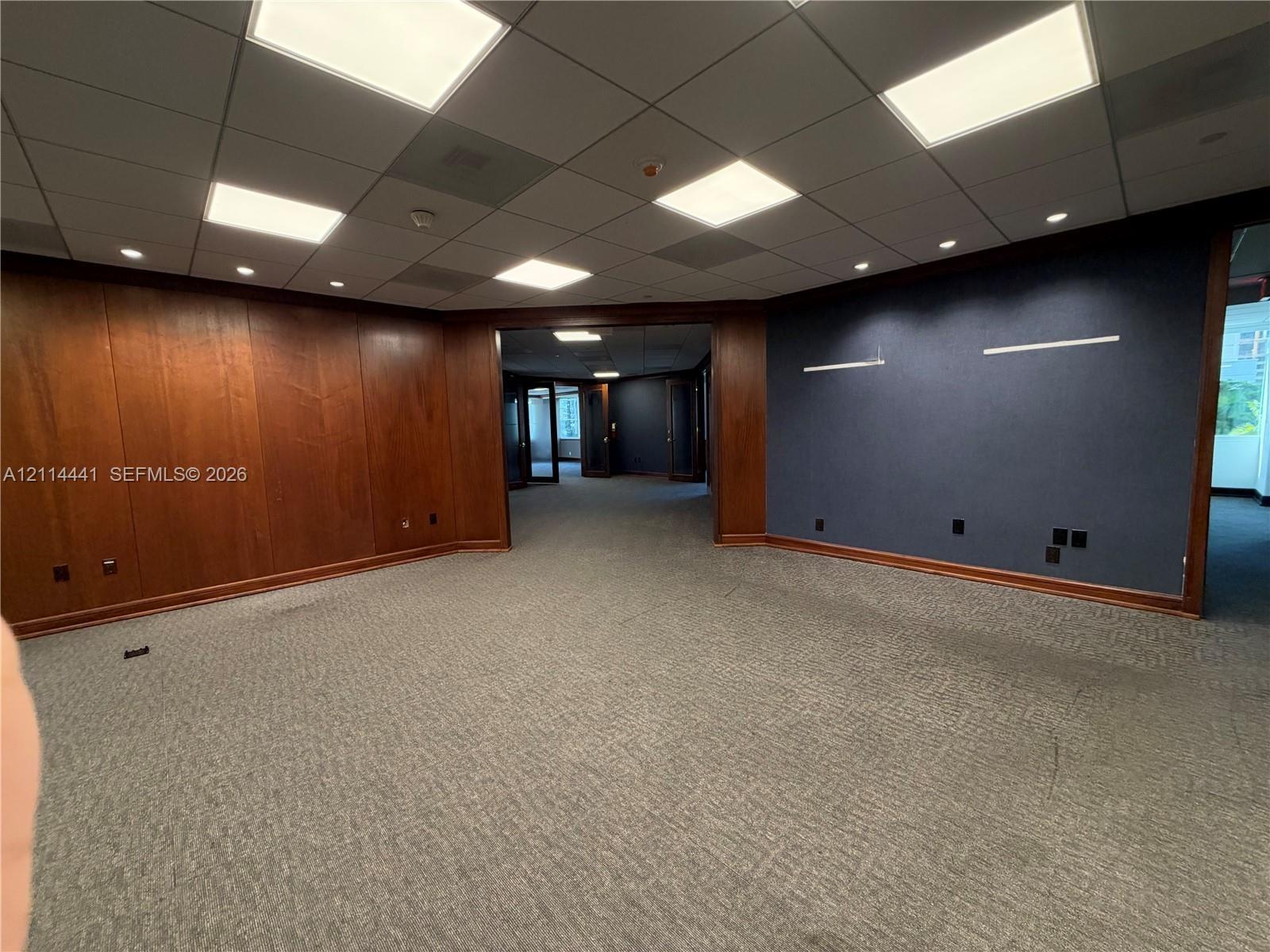 Wood-paneled wall accents, suspended grid ceiling with recessed lighting, and textured wall finish