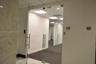 Frameless glass entry door featuring brushed metal hardware, suspended acoustic tile ceiling with recessed lighting, and stone-tiled foyer wall