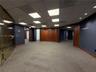 Commercial office space featuring high-contrast wood paneling, drop ceiling with recessed panel lighting, floor-to-ceiling glass partition with brass 
