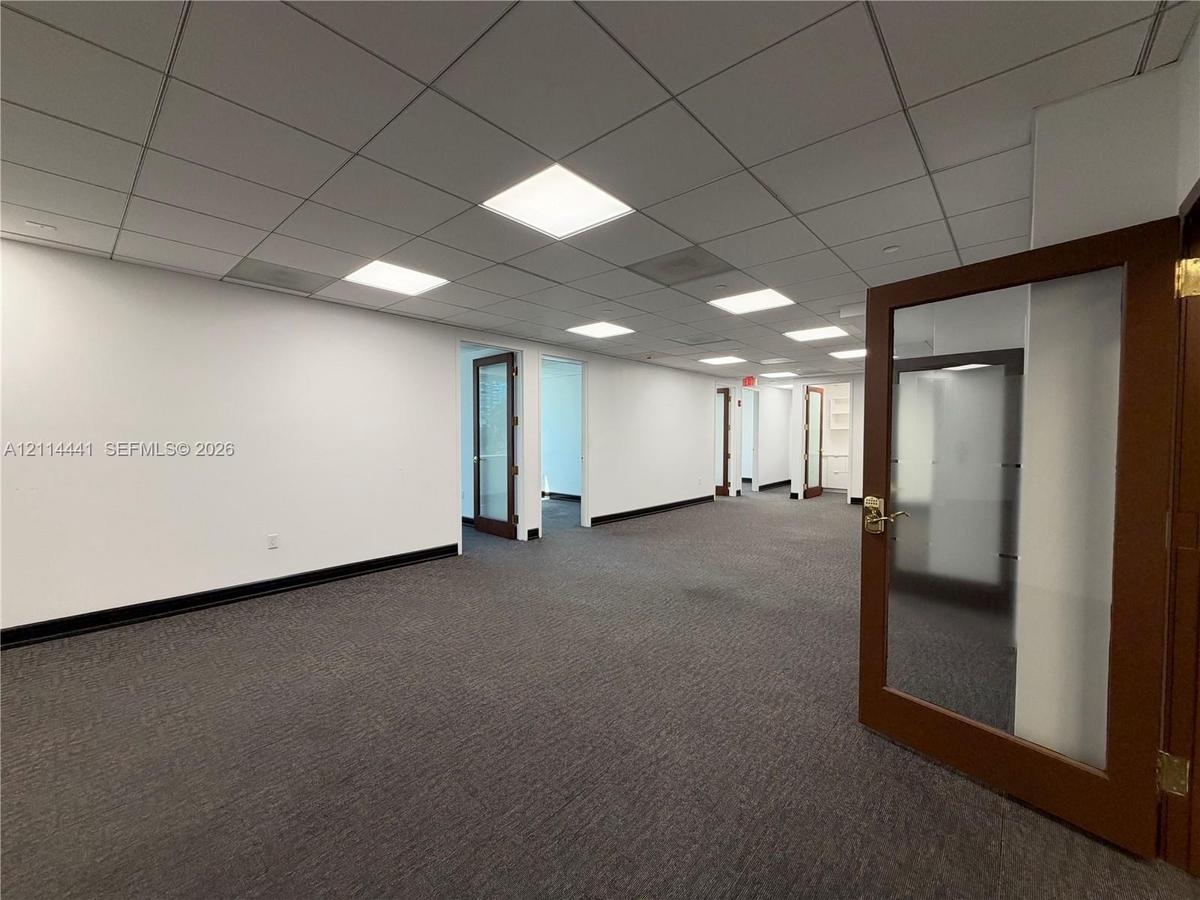 Expansive interior space featuring a drop ceiling with recessed lighting, wall-to-wall carpeting, and wood-framed doors with glass panels