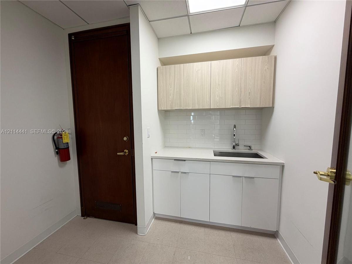 Kitchenette area featuring white cabinetry, wood-finish upper cabinets, solid-surface countertops, a tiled backsplash, and an integrated sink