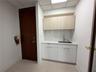 Kitchenette area featuring white cabinetry, wood-finish upper cabinets, solid-surface countertops, a tiled backsplash, and an integrated sink