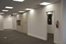 Expansive open-plan area featuring a drop ceiling with recessed panel lighting, neutral-toned carpeting, built-in light-finish cabinetry with integrat