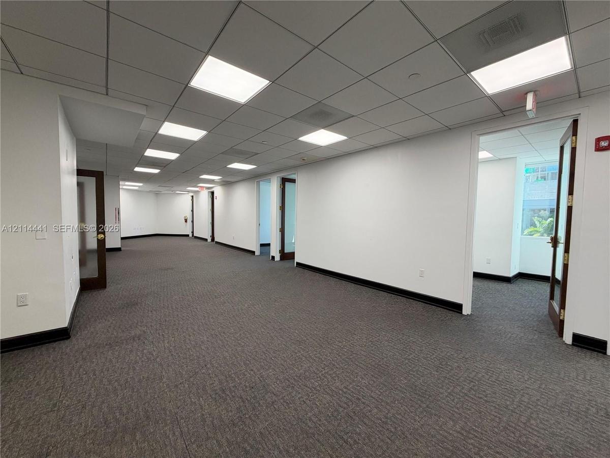 Open interior space featuring commercial-grade carpeting, recessed grid ceiling with integrated lighting, and multiple wood-trimmed glass panel doors