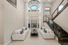 Two-story height ceiling with expansive windows, custom iron-frame chandelier, and staircase featuring dark wood finishes and glass railing panels