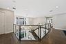 Open mezzanine landing featuring wood-finish flooring, glass panel railing with dark metal framing, recessed lighting, and a multi-tiered circular cha