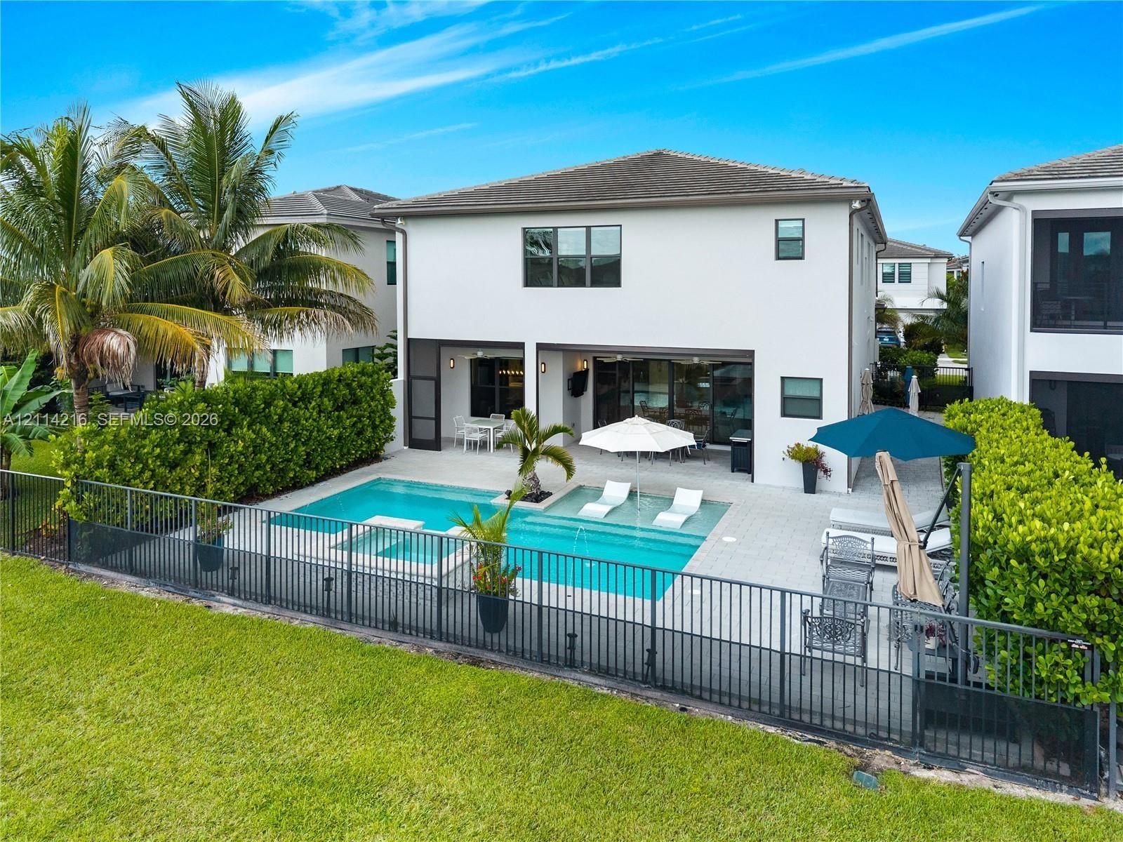 Rear exterior featuring a swimming pool with a sun shelf, integrated spa, paved pool deck, and black aluminum perimeter fencing