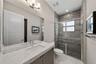 Vanity with light-toned stone-finish countertop and integrated rectangular basin, full-width mirror, glass-enclosed shower with horizontal textured ti