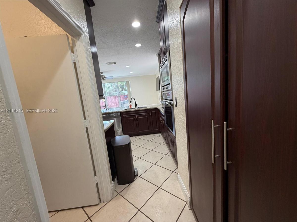 Kitchen featuring dark wood-finish cabinetry, built-in stainless steel double wall ovens, a gooseneck faucet, and diagonal-set tile flooring