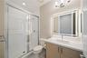 Bathroom featuring a walk-in shower with a glass enclosure, wood-finish vanity with a stone countertop, integrated undermount sink, and a modern LED-b
