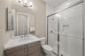 Bathroom featuring a wood-finish vanity with a stone countertop, an integrated rectangular sink, a glass-enclosed shower with subway tile surround, an