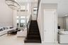 Double-height ceiling, large multi-pane windows, statement ring chandelier, staircase with wood-finish treads and a dark metal railing, and light-tone