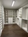 Walk-in closet featuring extensive built-in white cabinetry, integrated drawer banks, adjustable shelving, chrome hardware, and wood-finish flooring