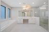 Bathroom featuring a walk-in shower with glass enclosure, soaking tub with tile surround, white cabinetry, integrated vanity, and decorative pendant l