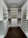 Custom walk-in closet featuring extensive white built-in shelving, multiple integrated storage drawers with brushed nickel hardware, and dark wood-fin