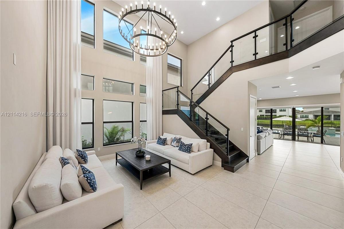 Two-story foyer featuring a floor-to-ceiling window wall, a modern multi-tier circular chandelier, and a custom staircase with glass panels and dark w