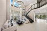 Two-story foyer featuring a floor-to-ceiling window wall, a modern multi-tier circular chandelier, and a custom staircase with glass panels and dark w