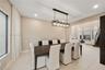 Open-concept interior featuring light-toned tile flooring, recessed ceiling lighting, and a linear multi-bulb metal chandelier