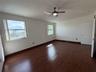 Spacious room featuring wood-finish flooring, vaulted ceilings, a central ceiling fan with integrated lighting, and multiple windows