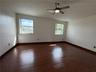 Spacious room featuring wood-finish flooring, neutral wall tones, two windows, and a ceiling fan with integrated lighting