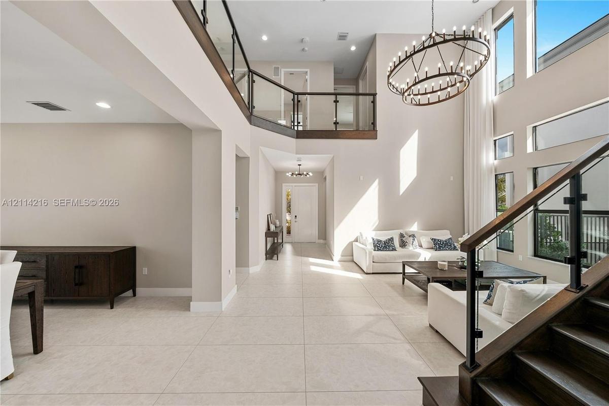 Double-height ceiling, open-concept floor plan with large-format tile flooring, staircase with dark wood treads and glass railings, multi-tiered circu