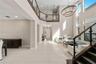 Double-height ceiling, open-concept floor plan with large-format tile flooring, staircase with dark wood treads and glass railings, multi-tiered circu