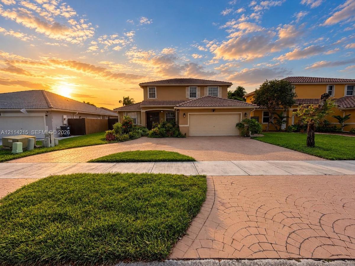 Two-story exterior featuring a decorative paved driveway, tiled roof, and manicured landscaping