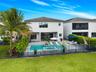 Rear exterior featuring a swimming pool with integrated spa, a paver patio, metal perimeter fencing, and established privacy hedges