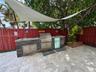 Outdoor kitchen featuring a stacked stone exterior, integrated stainless steel grill, drop-in sink, and stone paver patio