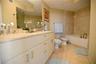 Double vanity with stone countertop, undermount sinks, and polished chrome faucets, featuring a full-width mirror, tile flooring, and a tiled shower-t