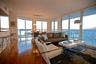 Open-concept interior featuring floor-to-ceiling glass walls, expansive water scenery, wood-finish flooring, and a built-in kitchen breakfast bar