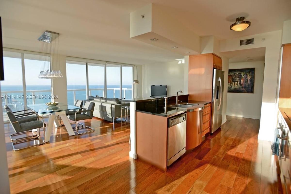 Wood-finish flooring, kitchen island with dark solid-surface countertop, stainless steel appliances, and floor-to-ceiling windows