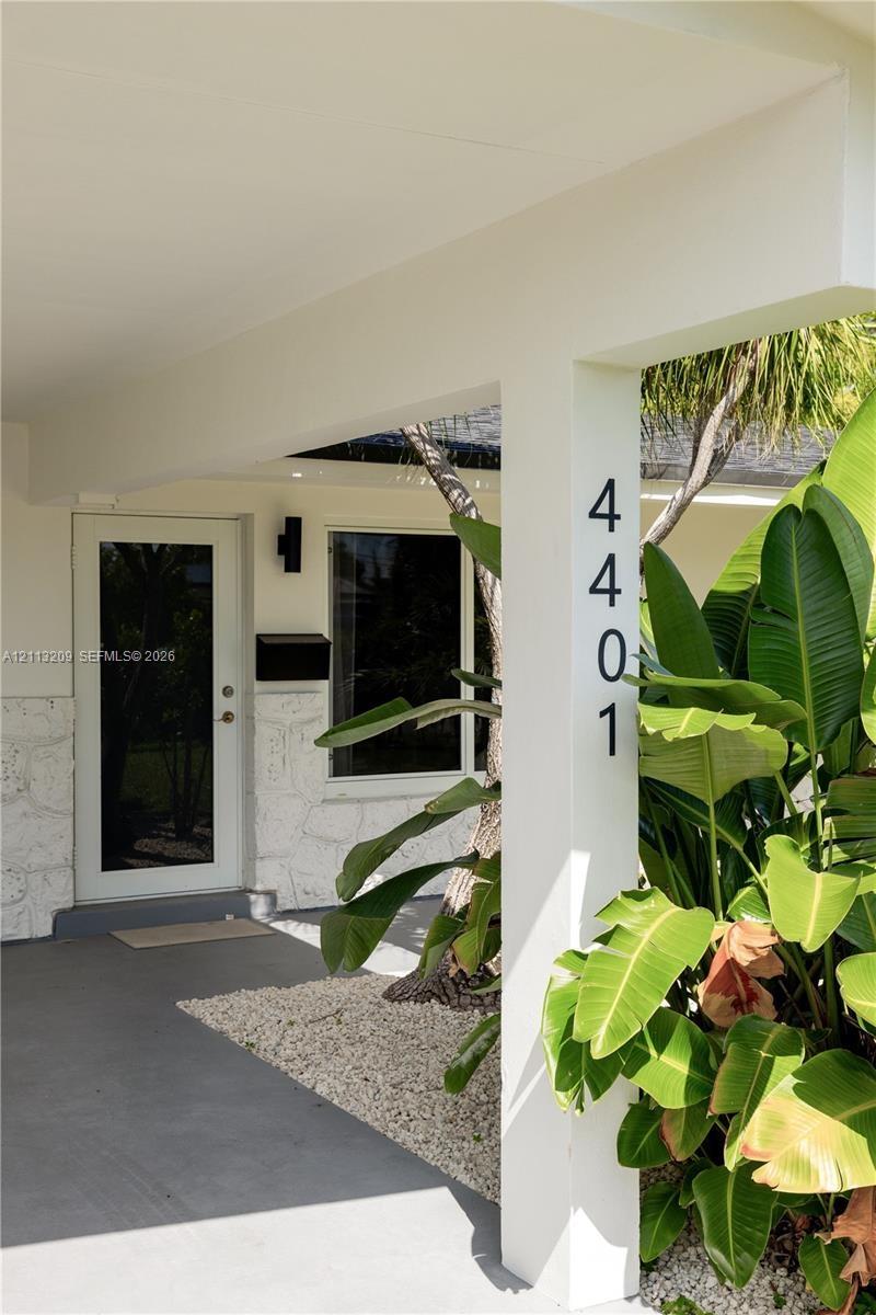 Covered entryway featuring light-toned stone masonry facade, full-glass panel entry door, matte black wall-mounted fixtures, and minimalist vertical a