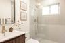 Bathroom featuring a fluted wood-finish vanity with a white countertop, brushed gold faucet, glass-enclosed shower with tiled walls, and a minimalist 