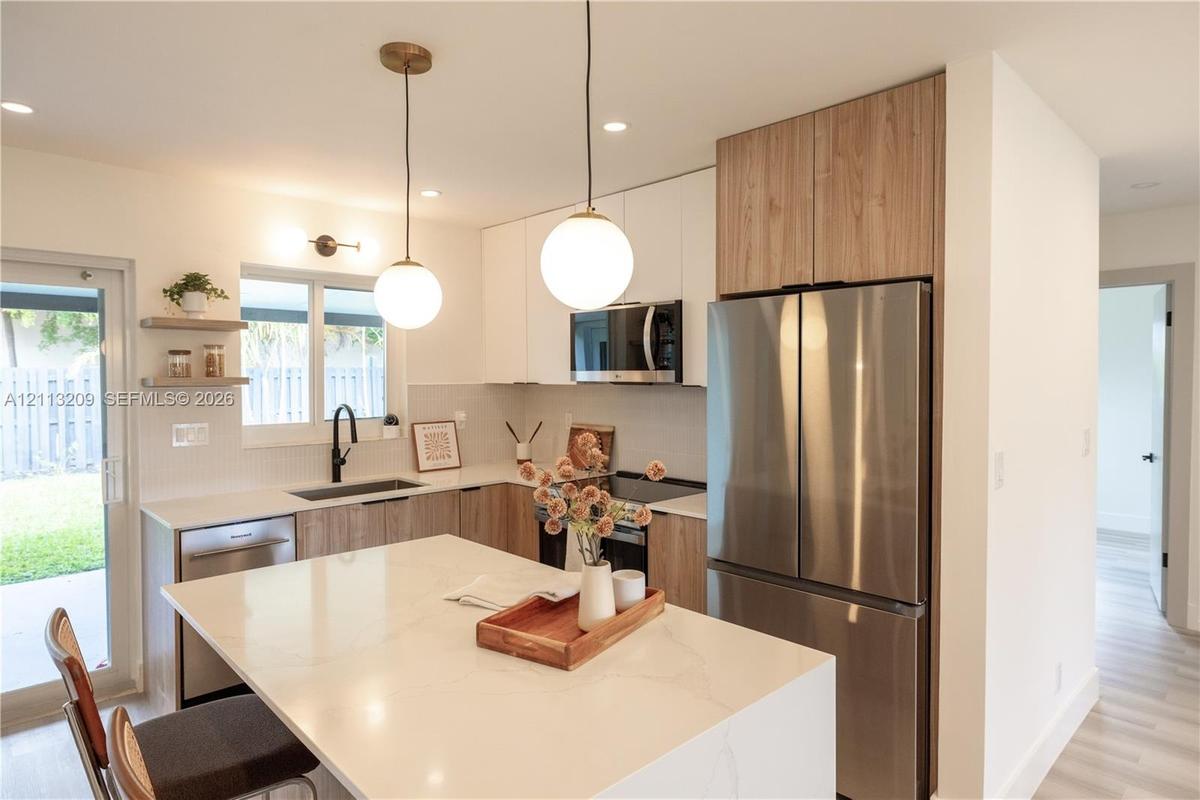 Kitchen featuring a stone-surface island, two-tone cabinetry, stainless steel appliances, matte black plumbing fixtures, and globe pendant lighting