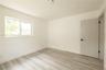 Neutral-toned interior space featuring wood-finish flooring, recessed lighting, a horizontal sliding window, and a solid-panel door with matte black h