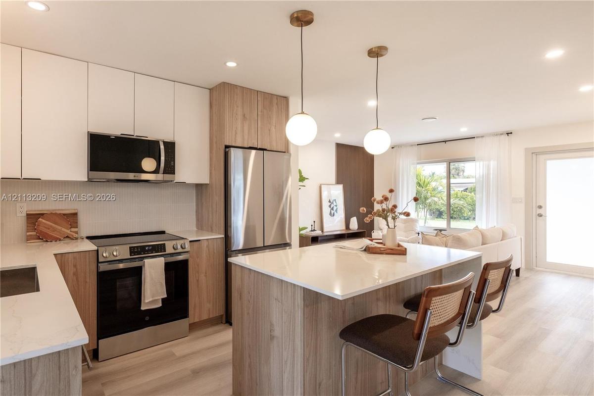 Kitchen featuring wood-finish cabinetry, white slab countertops, stainless steel appliances, central island with seating, and glass globe pendant ligh