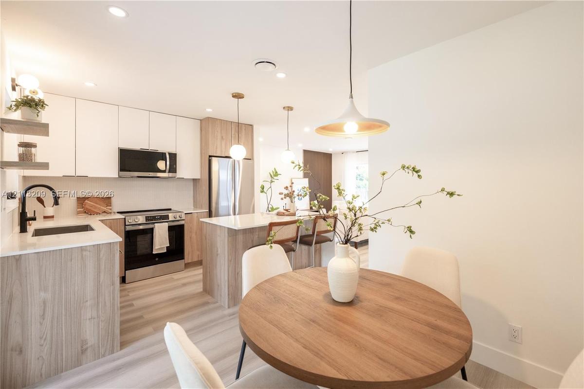 Kitchen featuring two-tone cabinetry, quartz countertops, stainless steel appliances, wood-finish flooring, and pendant lighting