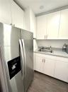 Stainless steel side-by-side refrigerator, white cabinetry with brushed metal hardware, solid-surface countertop, and integrated sink with faucet fixt