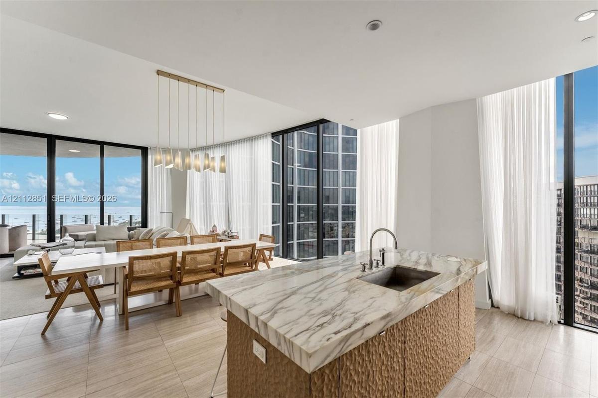 Kitchen island with stone countertop, undermount sink, and textured cabinetry, complemented by floor-to-ceiling glass windows and recessed lighting
