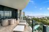 Covered outdoor balcony featuring large-format stone-finish tile flooring, floor-to-ceiling glass doors, and a glass-paneled railing overlooking the s