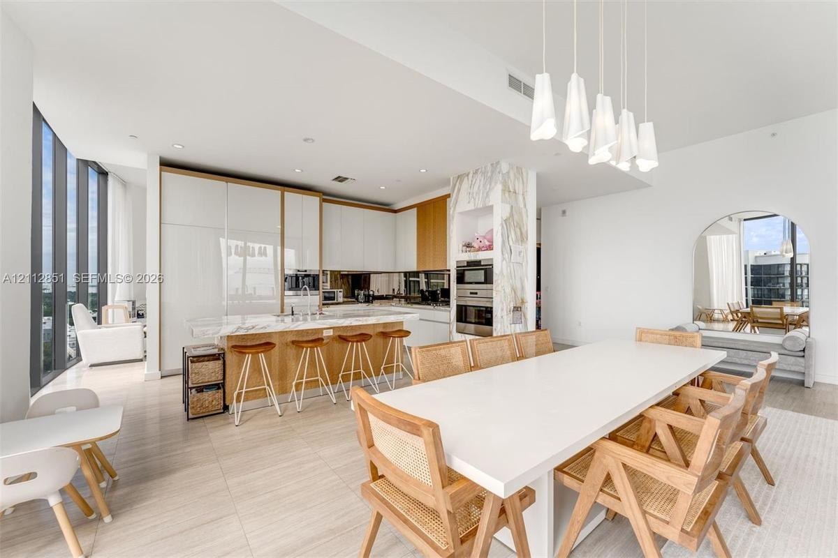 High-gloss cabinetry, stone-surface kitchen island, built-in stainless steel double ovens, floor-to-ceiling windows, and contemporary multi-pendant li